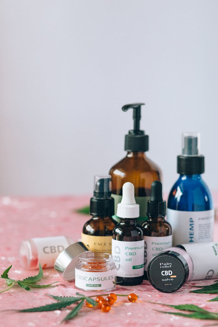 A variety of CBD and hemp products displayed on a pink surface with scattered leaves.