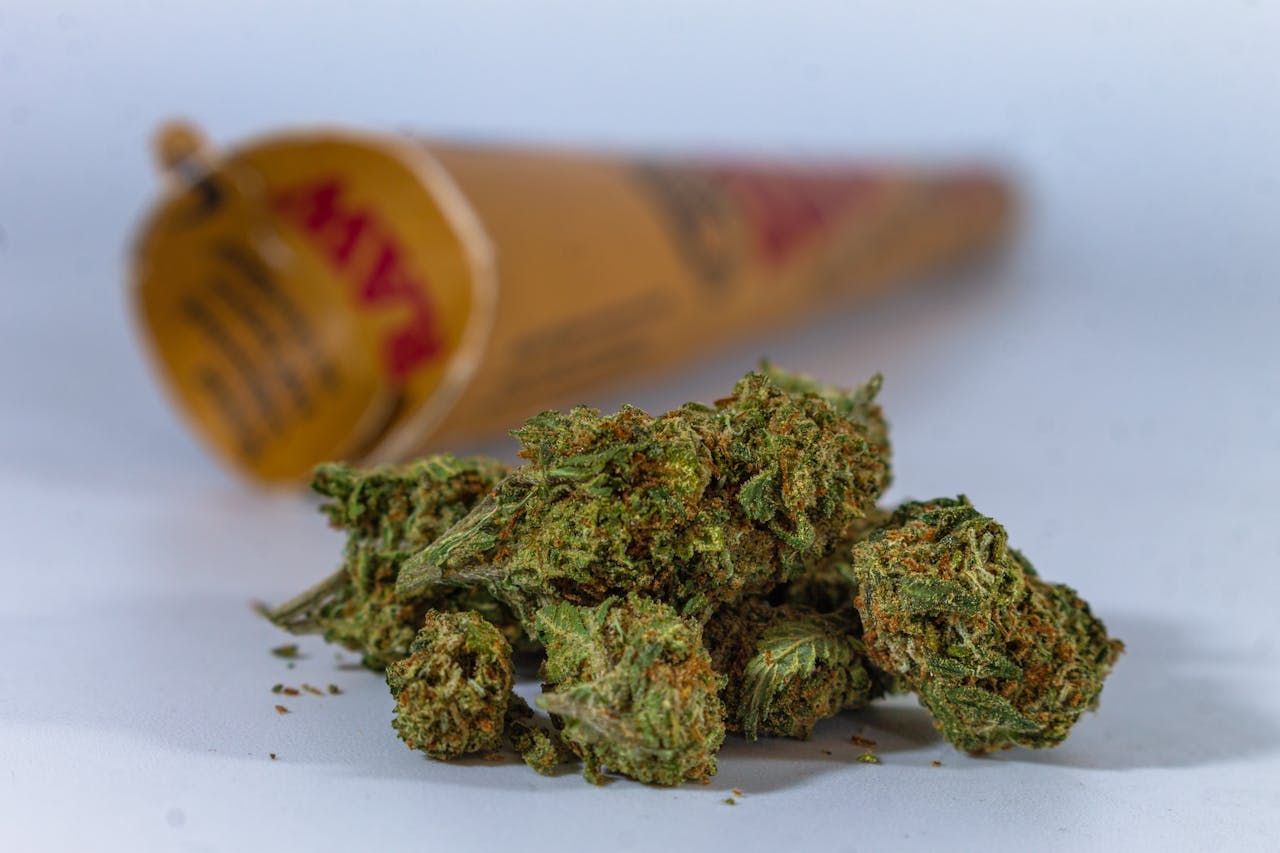 Close-up of cannabis buds with a blurred rolling paper in the background.